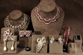 An elegant display of fine jewelry, including necklaces, earrings, brooches, and rings, adorned with red and white gemstones, set against a velvet-lined showcase.